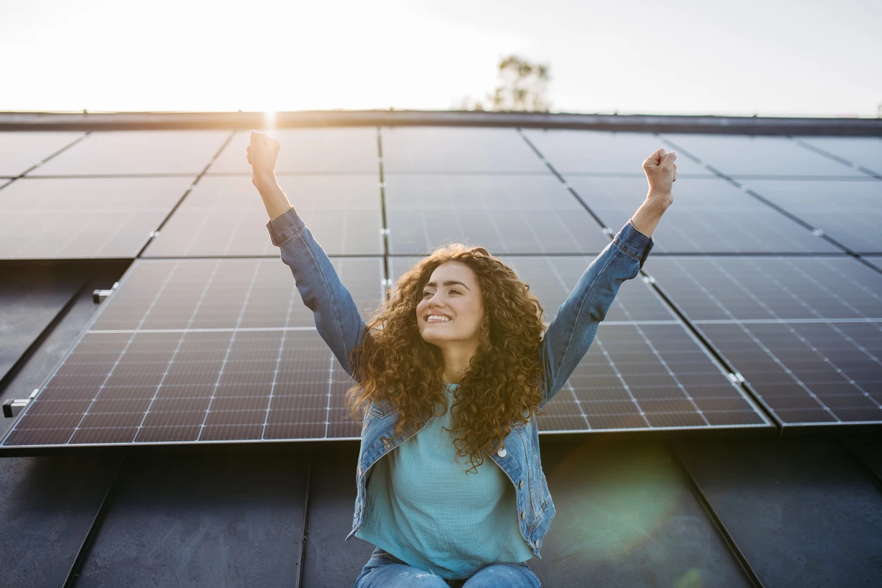 Mulher feliz celebrando energia renovável com painéis solares ao fundo, simbolizando sustentabilidade e uso de energia solar para um futuro mais limpo.