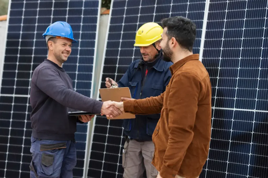 Engenheiros e técnicos no campo de energia solar, fazendo um acordo de parceria ou fechamento de projeto, com painéis solares ao fundo.