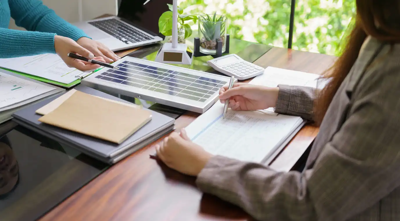Equipe de trabalho discutindo sobre energia solar em reunião de negócios, com painéis solares e laptops na mesa, promovendo investimentos em energia renovável.
