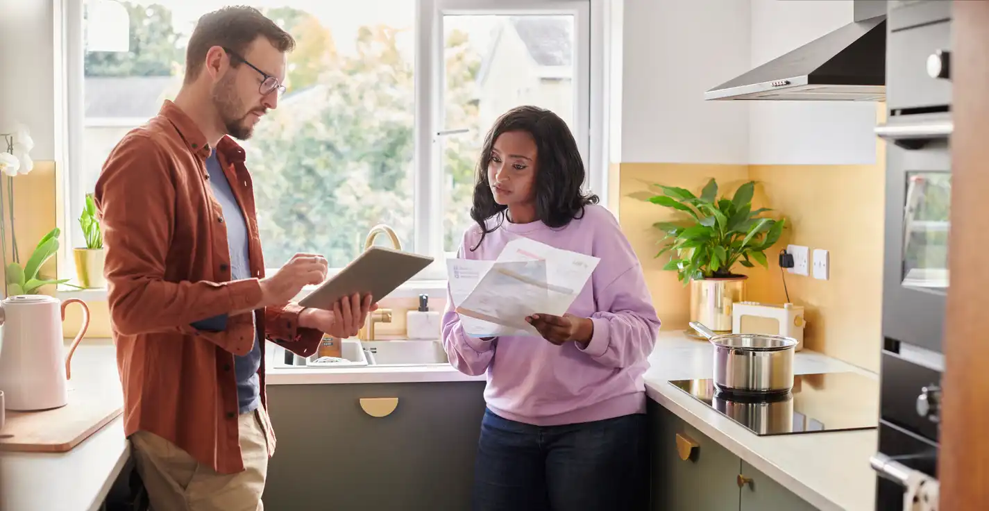 Casal conversando na cozinha moderna com plantas e utensílios domésticos, discutindo um projeto ou planejamento juntos.