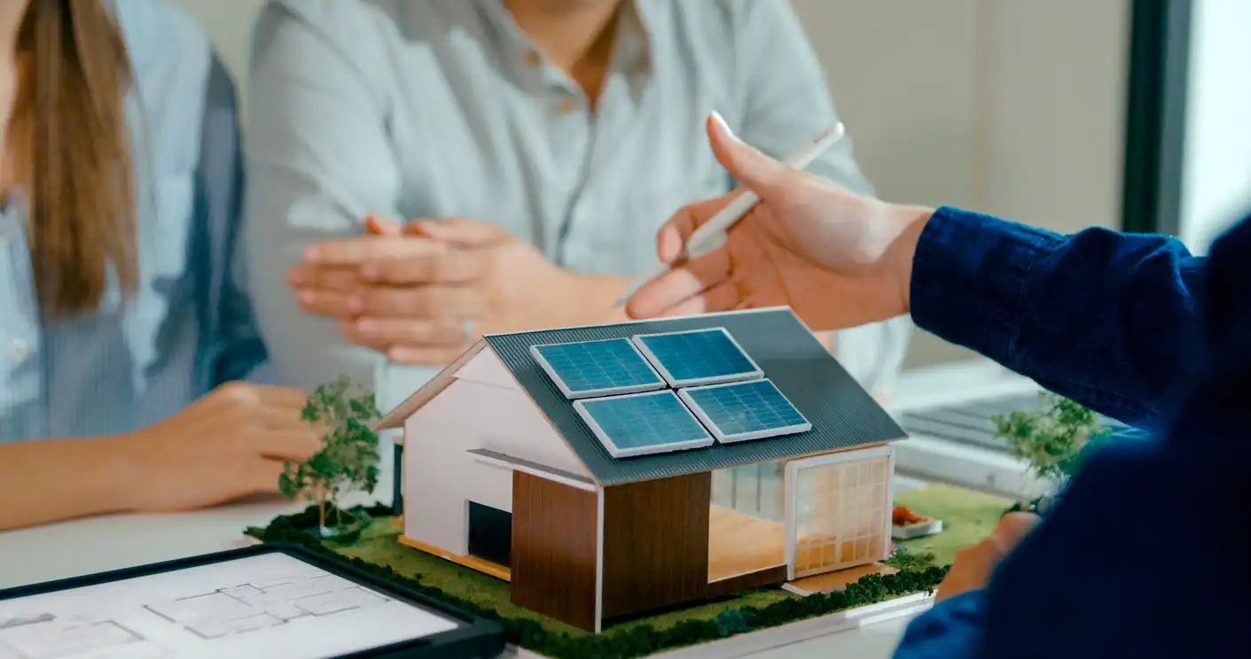 Pessoas participando de uma reunião sobre energia renovável, apresentando um modelo de casa com painéis solares no telhado para sustentabilidade.