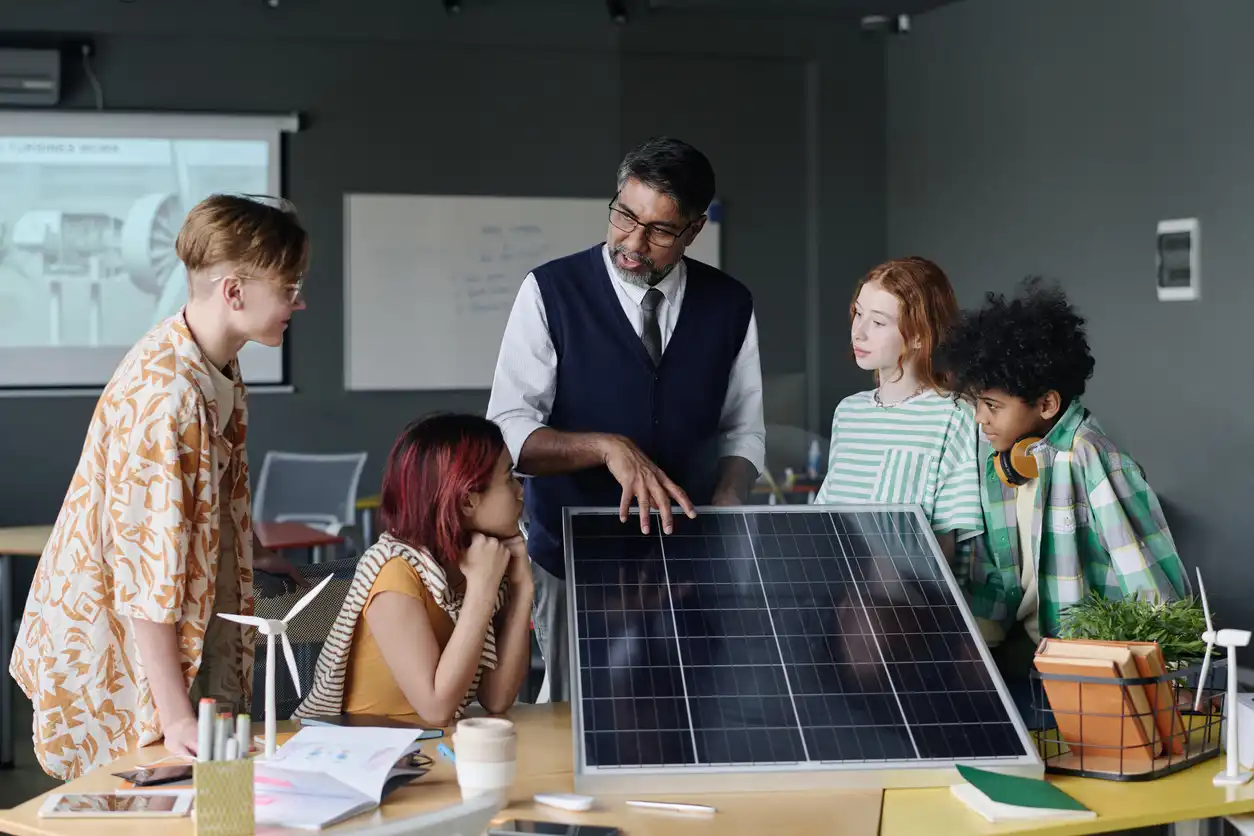 Professor ensinando grupo de crianças sobre energia solar em sala de aula com painel solar e projetos sustentáveis.