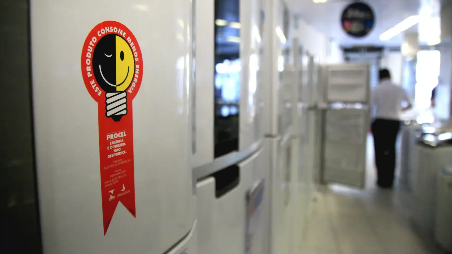 Imagem de uma geladeira em uma lavanderia automática, com etiqueta de eficiência energética e ambiente bem iluminado ao fundo.