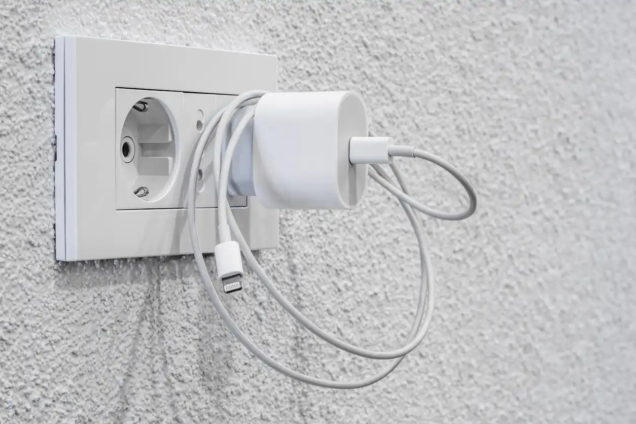 Imagem de uma tomada elétrica com carregador conectado e cabos USB, símbolo de carregamento e energia em ambiente residencial ou de escritório.